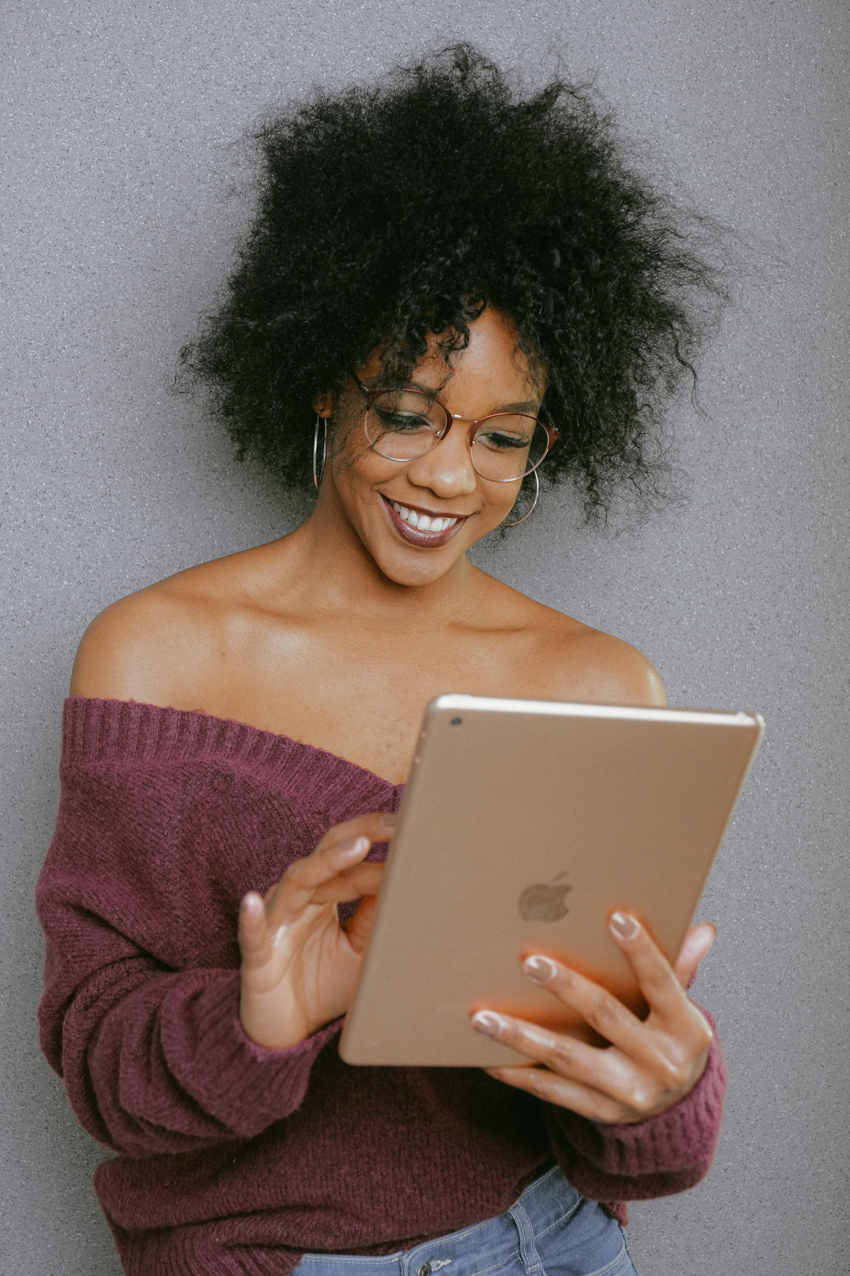 A young woman with curly hair smiling while using a tablet indoors.