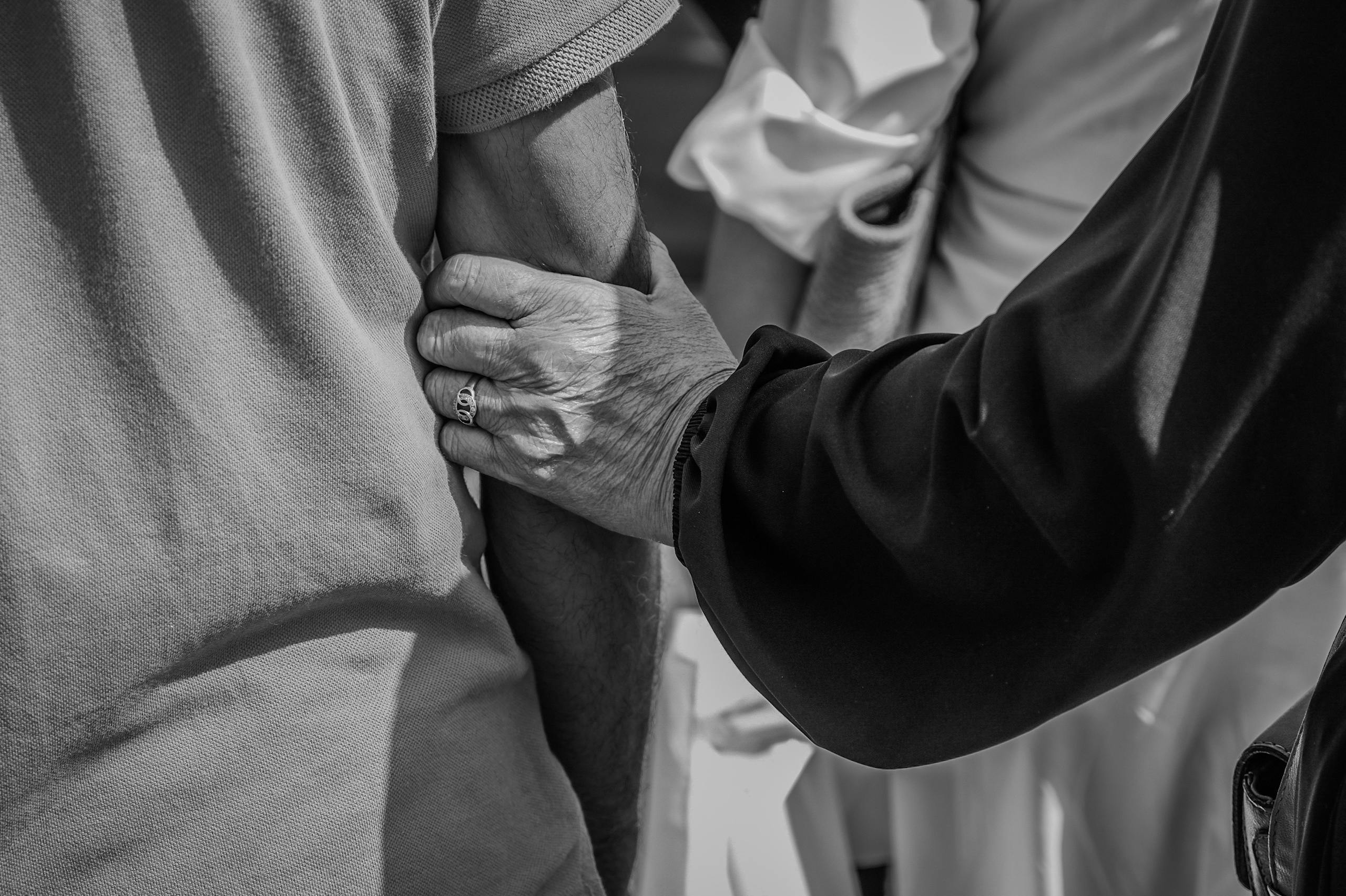 Black and white photo of an elderly pair holding arms, symbolizing support and care.