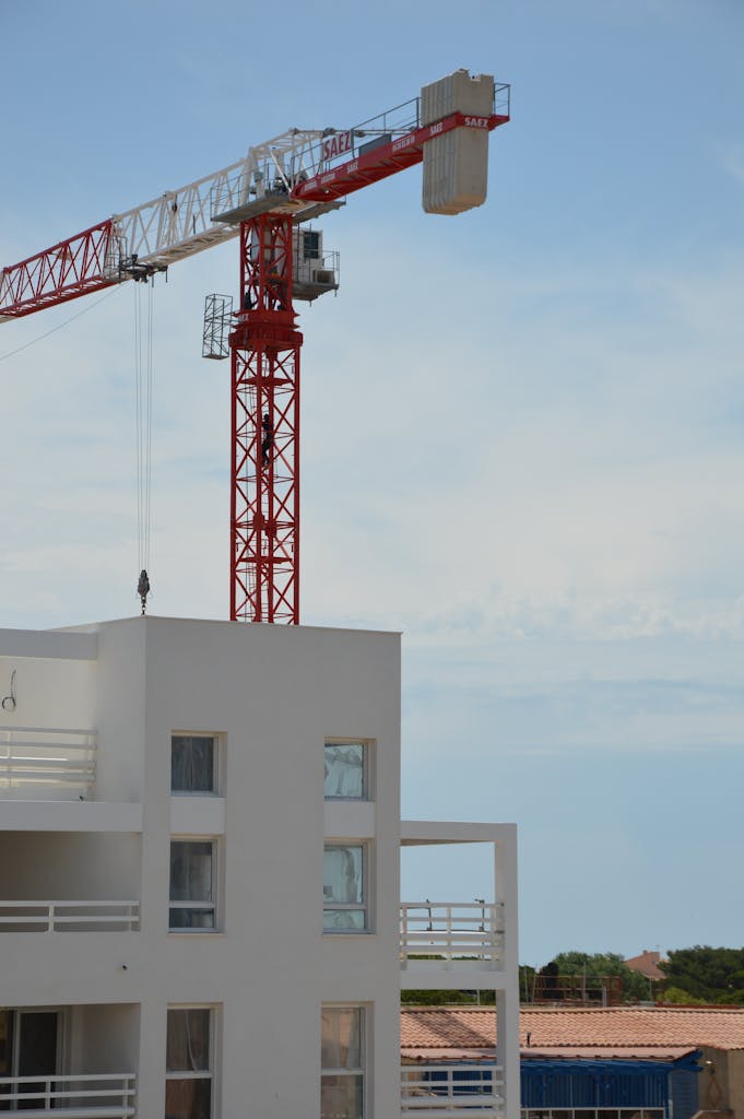 View of a modern building under construction with a towering red crane against the sky.