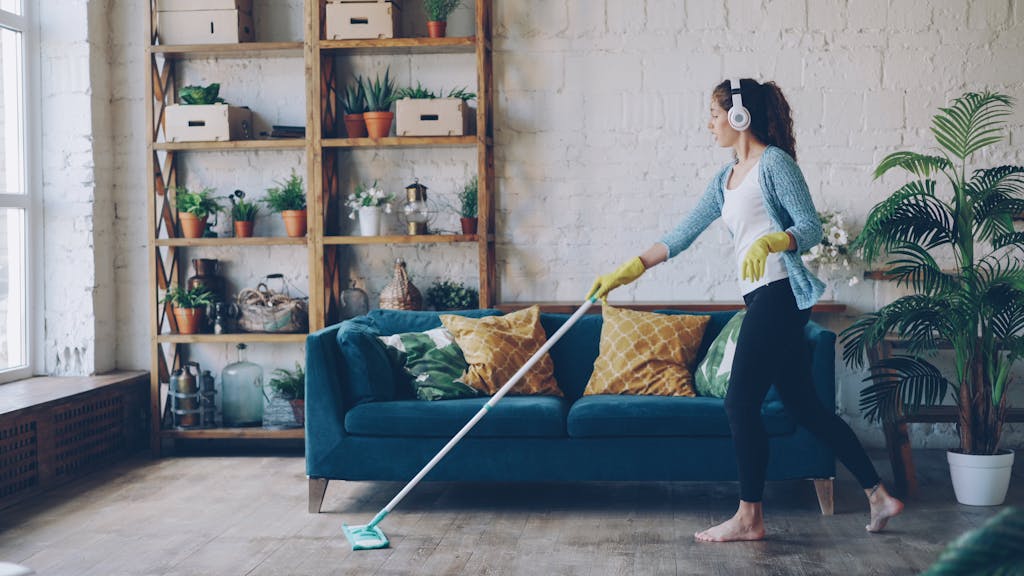 Woman wearing headphones and gloves while mopping a stylish indoor living room.